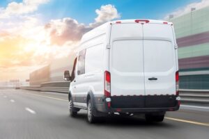 White mini bus is moving motion blur along city highway bypass road with beautiful sky before sunset. Fast express delivery service of goods and parcels.